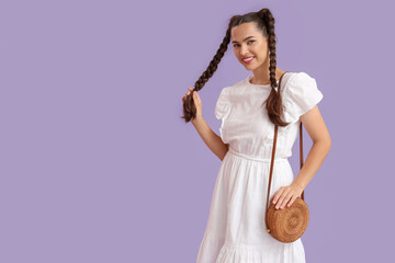 Poster - Beautiful young happy stylish woman with braids holding wicker bag on purple background