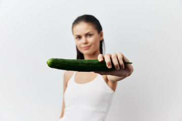 Canvas Print - Woman holding a cucumber in a playful manner with a bright and minimalistic background The focus is on the subject s expression and the vibrant green color of the cucumber