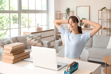 Poster - Happy female student in headphones with books and laptop studying at home