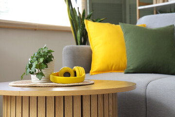 Wall Mural - Wooden coffee table with houseplant and modern headphones in living room, closeup