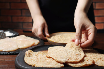 Wall Mural - Woman making schnitzel at wooden table, closeup