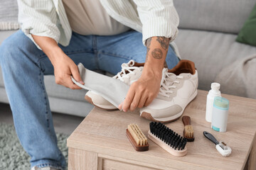 Wall Mural - Young man cleaning sneakers on table at home