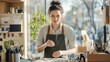 © Sumet - A young woman in an apron focuses on her craft at a bright studio filled with art supplies and natural light.