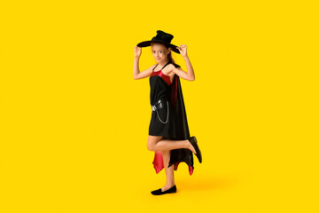 Teenage girl dressed for Halloween as witch on yellow background