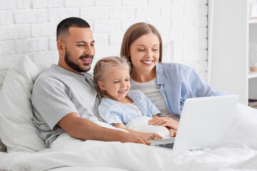 Sticker - Cute little girl with her parents using laptop under blanket in bedroom