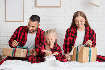 Sticker - Happy parents with their little daughter unwrapping Christmas presents in bedroom