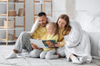 © Pixel-Shot - Happy parents with their little daughter reading book under blanket in bedroom