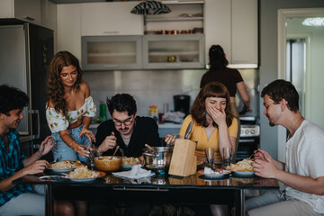 Wall Mural - A lively group of friends shares a meal in a cozy kitchen setting. Laughter and joy fill the room as they enjoy each other's company.