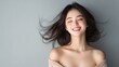 © PhirakAi02 - A joyful woman with flowing hair smiles radiantly against a soft gray background, embodying happiness and beauty.