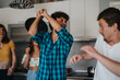 © qunica.com - Group of friends in a kitchen engaging in a playful game, using a pan as a part of the fun, with expressions of surprise and laughter.