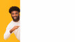 © Prostock-studio - Empty space for advertising. Cheerful black guy pointing at big blank board, orange background, panorama