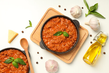 Pans with Bolognese sauce and ingredients on white background, top view