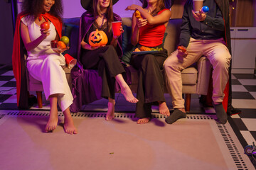 An African American woman and a white woman celebrate with coworkers, drinking, having fun, and smiling together at a lively Halloween night party filled with joy and laughter.