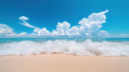 A series of rolling waves gently breaking on a sandy beach, with a vibrant blue sky and fluffy clouds above.