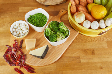 A wooden cutting board arranged with an assortment of fresh vegetables, cheeses, and peppers, ready for cooking or meal preparation