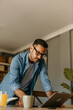 © La Famiglia - A man working from home over a laptop standing over the wooden table.
