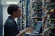 © ZHIJIAN - A female african american IT engineer works in a data center, analyzing network configurations on her laptop while surrounded by server racks and numerous connected cables