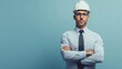 © Elmira - A male engineer stands confidently with arms crossed, wearing a formal shirt and tie along with a white construction helmet, against a soft blue backdrop