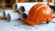 © Business Image - Construction planning essentials: orange helmet and blueprints for engineering projects