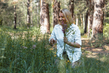 a young beautiful girl in a shirt and shorts is picking flowers in a clearing in the forest