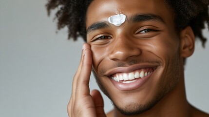 Young man applying moisturizer on his forehead while smiling at the camera in a bright indoor setting