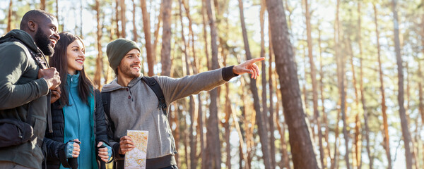 Happy multiracial hikers found right way, holding map and looking at free space at forest