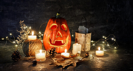 Halloween holiday. Pumpkin decoration with burning candles and jack-o-lantern face on dark rustic background copyspace place for text