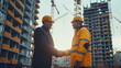 © visoot - Two people in suits and helmets shake hands against the background of the construction of a multi-story residential complex. Generative AI.