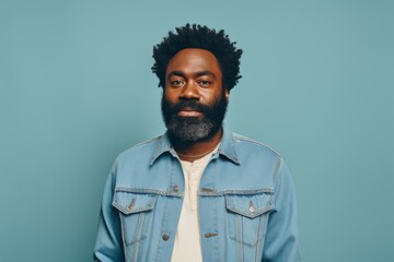 Wall Mural - Portrait of a content afro-american man in his 40s sporting a rugged denim jacket in front of pastel teal background