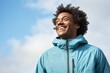 © Markus Schröder - Portrait of a grinning afro-american man in his 30s wearing a lightweight packable anorak while standing against soft blue background