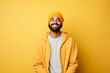 © Markus Schröder - Portrait of a blissful indian man in his 20s sporting a trendy beanie while standing against soft yellow background