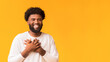 © Prostock-studio - Smiling african american guy placing hands together next to heart, expressing his pleasure, orange background