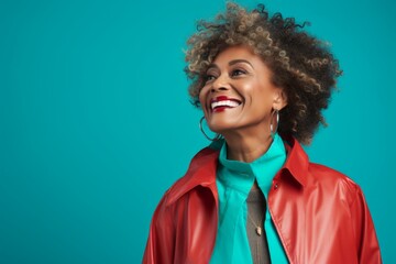 Wall Mural - Portrait of a content afro-american woman in her 50s wearing a vibrant raincoat in front of soft teal background