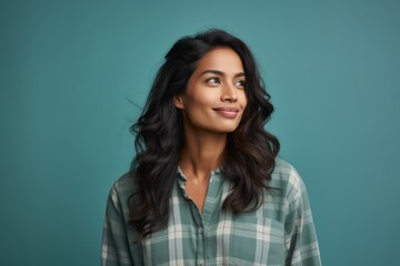 Poster - Portrait of a glad indian woman in her 20s wearing a comfy flannel shirt isolated in soft teal background