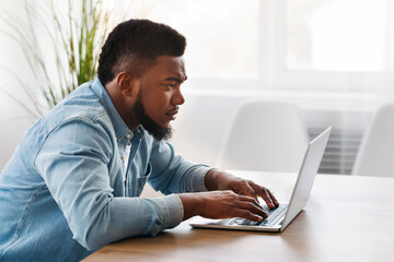 Poster - Working on new project. Concentrated young african worker using laptop in office, side view with free space