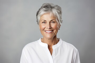 Poster - Portrait of a grinning woman in her 60s wearing a classic white shirt in front of soft gray background