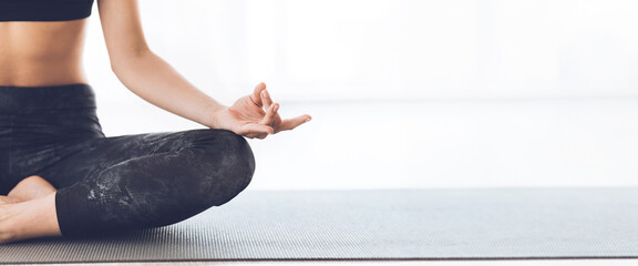 Wall Mural - A woman sits cross-legged in a yoga pose, practicing meditation with a calm expression in a sunlit studio, cropped, copy space