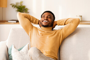 Poster - Weekend At Home. Happy Afro Man Relaxing Sitting On Sofa Holding Hands Behind Head Indoor. Copy Space