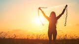 A woman stands in a field at sunset, triumphantly breaking chains overhead with raised arms, symbolizing freedom and empowerment