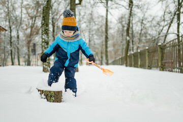 Wall Mural - Adorable little boy having fun on snowy winter day. Cute child wearing warm clothes playing in a snow.