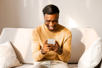 Aufkleber - Mobile Gaming. Excited Afro Guy Using Cellphone Playing Games Sitting On Couch At Home.