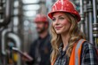© Nataliia_Trushchenko - A woman wearing a hard hat and safety vest stands in front of a man. She is smiling and holding a tablet. Concept of professionalism and safety in the workplace