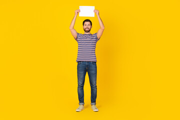 Sticker - Full length photo of good mood guy wear striped t-shirt jeans hold placard over head empty space isolated on yellow color background