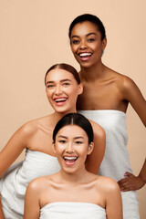 Three Happy Multicultural Girls In White Bath Towels Posing In Studio Over Gray Background. Vertical