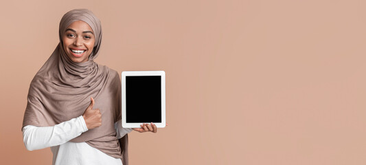 Poster - Great App. Positive black islamic girl in hijab holding digital tablet with black screen and showing thumb up gesture over yellow background, mockup