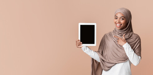 Poster - Smiling Afro Muslim Girl Pointing At Digital Tablet With Black Screen, Posing Over Yellow Background, Free space