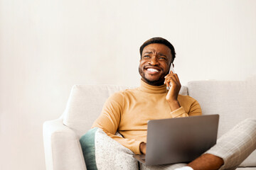 Aufkleber - Successful Entrepreneur. Happy Black Man Talking On Cellphone Working On Laptop Sitting On Couch Indoor. Selective Focus, Free Space