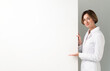 © Vitaliy - Female doctor standing and pointing on blank banner isolated on white background