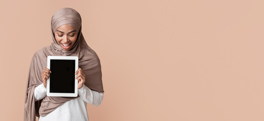 Poster - Overjoyed black muslim girl looking down at digital tablet with black screen in her hands, standing over yellow background, mockup