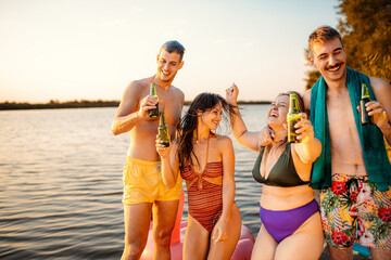 Wall Mural - Group of friends in swimsuit having fun standing on a pier drinking beer enjoying a summer day at the lake.